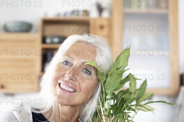 Elderly woman with long hair snuggles up to houseplant at home