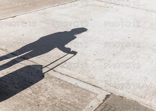 Shadow female tourist holding wheeled luggage asphalt