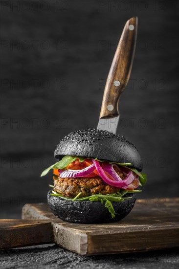 Front view veggie burger with black buns cutting board with knife