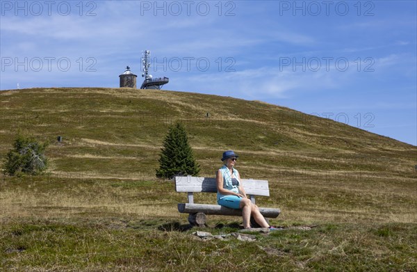 Hiker sitting on a bench on the Gerlitzen with view to the Kanzelhoehe