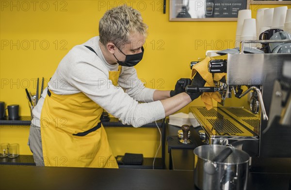 Side view male barista with medical mask cleaning coffee machine