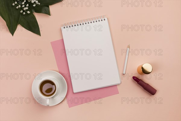 Blank spiral notepad pencil lipstick coffee cup leaves peach background