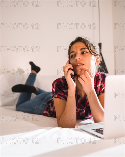 Beauty young woman working with laptop and mobile lying on a hotel room