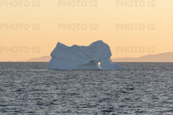 An iceberg floats in the rising morning sun off the mountains of the Greenland coast. Disko Bay