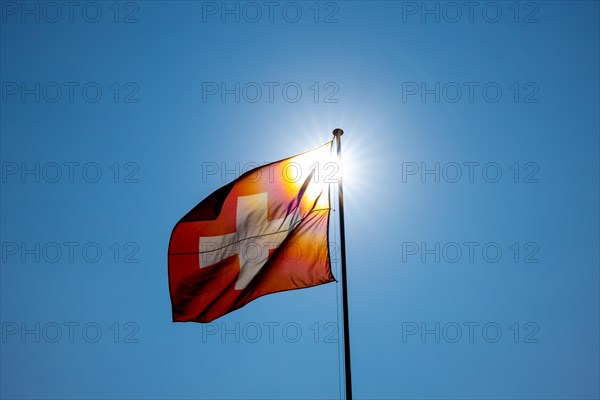 Beautiful Swiss Flag Against Blue Clear Sky and Sunbeam in a Windy Day in Switzerland
