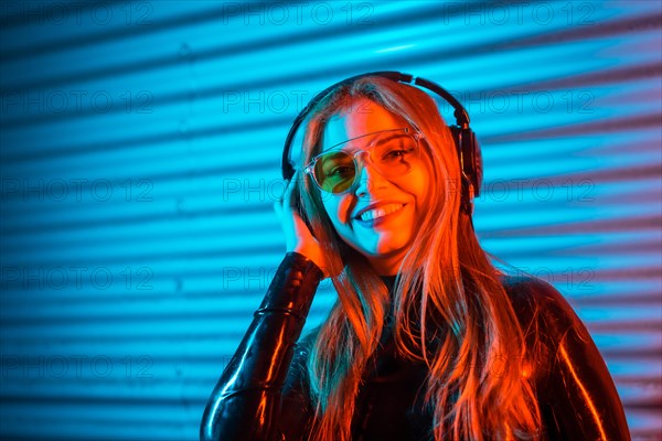 Smiley disc jockey using headphones in an urban space with blue and red neon lights