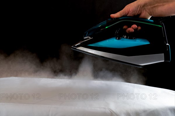 Woman ironing a white cloth by pouring steam from the iron on a black background