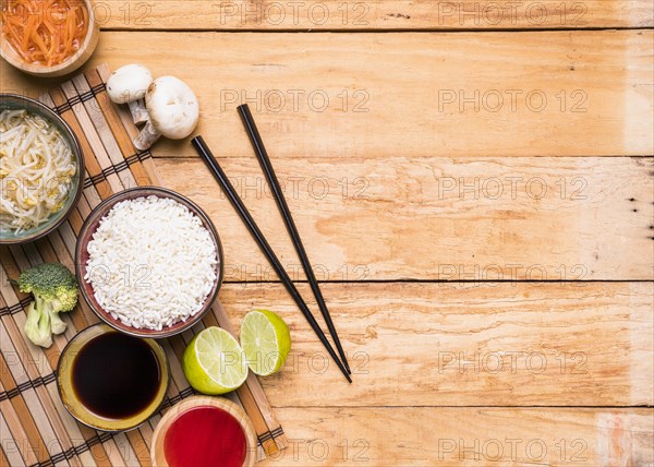 Elevated view mushroom sprout beans rice broccoli lemon sauce with chopsticks against wooden desk