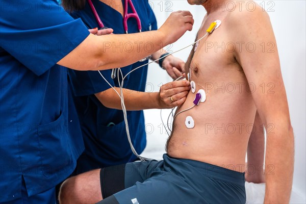 Cropped close-up photo of two cardiologists placing electrodes to a patient to perform a cardiovascular stress test