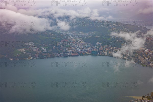 Aerial View over City and Lake Lugano in Valley with Mountainscape with Storm Clouds in Lugano
