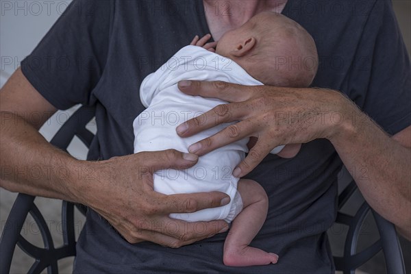 Newborn baby in the arms of the young grandfather