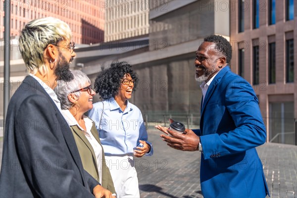 African businessman in blue suit talking with colleagues outdoors while drinking coffee and smiling