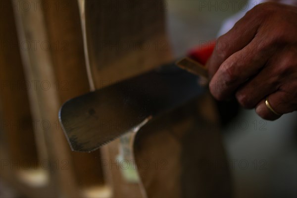 Senior violinmaker holding a tool chisel in workshop in Cremona