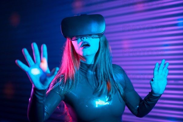 Surprised woman during an interactive game with VR goggles in an urban night space with neon lights
