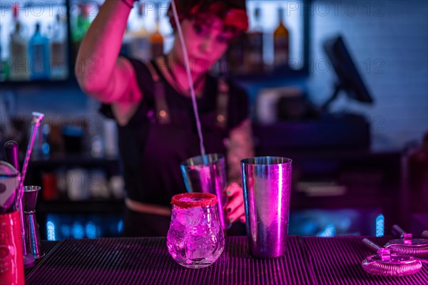 Bartender pouring alcohol to a mixer preparing a cocktail in the counter of a bar with neon lights