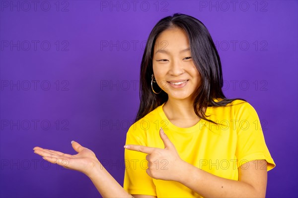 Studio photo with purple background of a positive chinese woman pointing to the side
