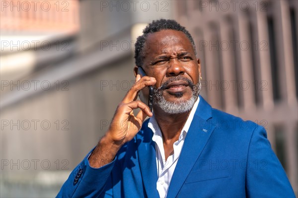 Mature african businessman in blue suit talking to the phone outdoors