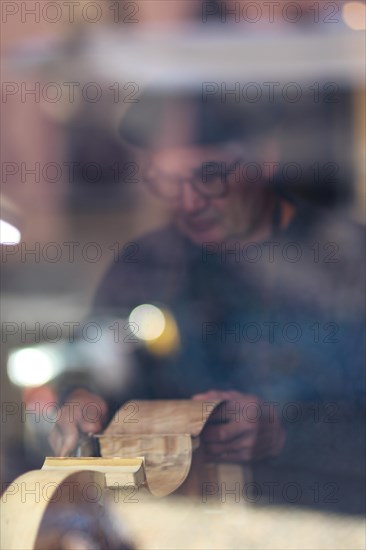 Senior expert luthier artisan violin maker carve sculpt chisel ribs of a new classical model cello in workshop Cremona Italy