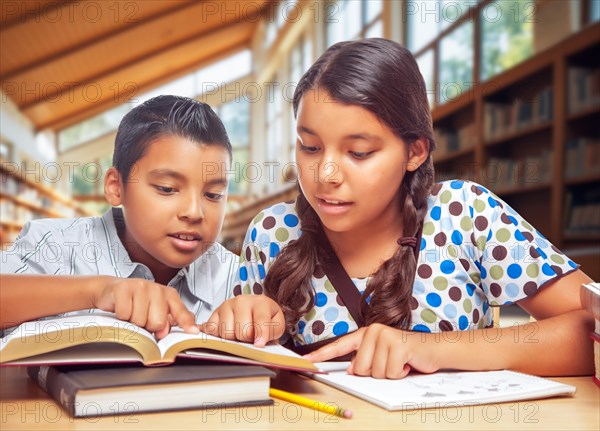 Two hispanic school kids studying with their books in a library