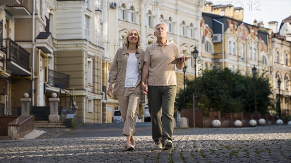 Front view elder couple out walk city with tablet