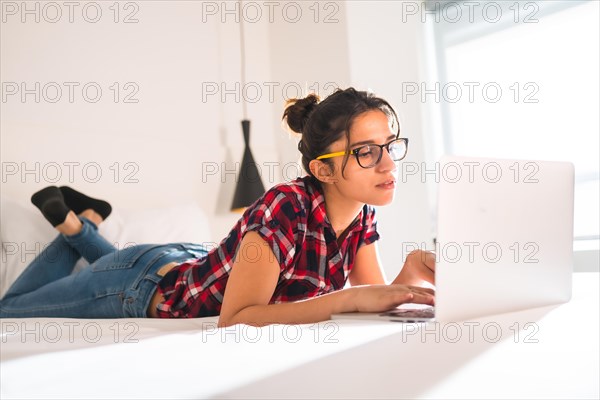 Side view of a young woman working with laptop lying on hotel bed