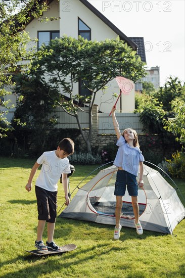 Girl catching butterflies with scoop net boy playing skateboard near tent camp