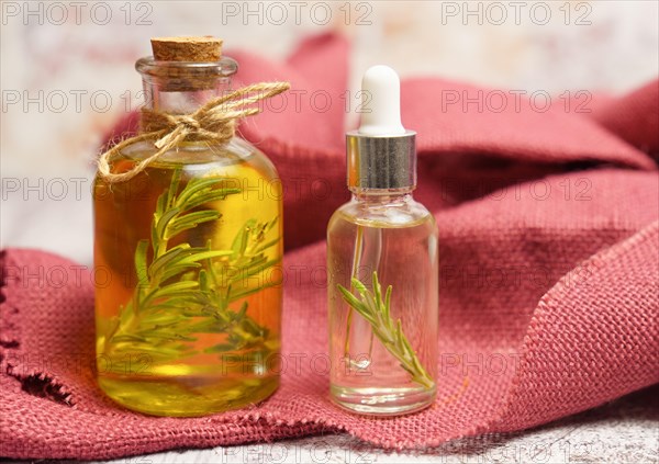 Bottle and dropper with rosemary oil with fresh twigs inside on a red cloth