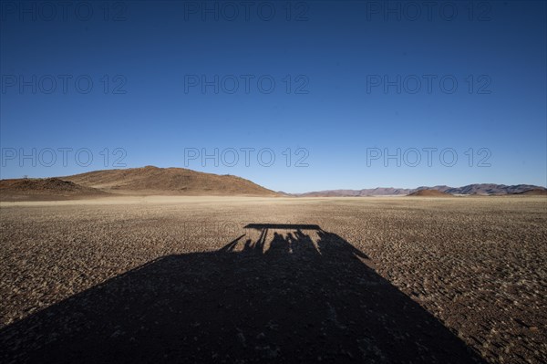 Shadow of safari vehicle in the Namib Desert with Tiras Mountains