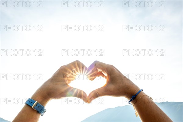 Woman Hands Making a Heart Shape Against the Sky with Sun and Sunbeam and Mountain in Switzerland