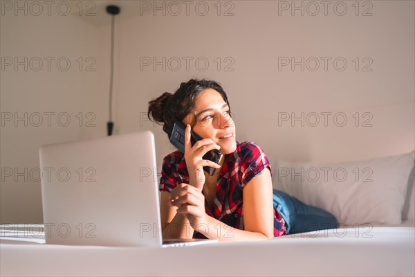 Young woman working on remote from an hotel room lying comfortable on the bed