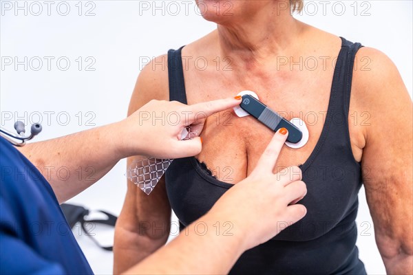 Female doctor putting woman with heart problems undergoing ECG Holter monitor test with innovative device on chest