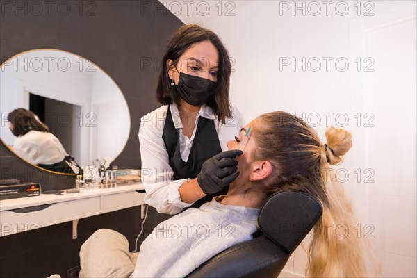 Professional brushing the eyebrows of a client sitting on a chair facing a mirror in at a beauty salon