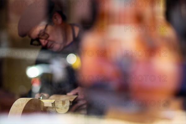 Senior expert luthier artisan violin maker carve sculpt chisel ribs of a new classical model cello in workshop Cremona Italy