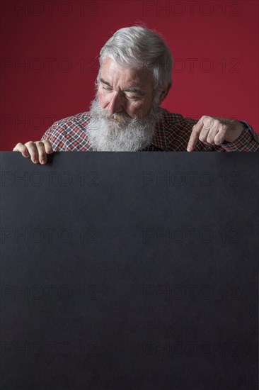 Close up senior man with grey beard pointing her finger blank black placard