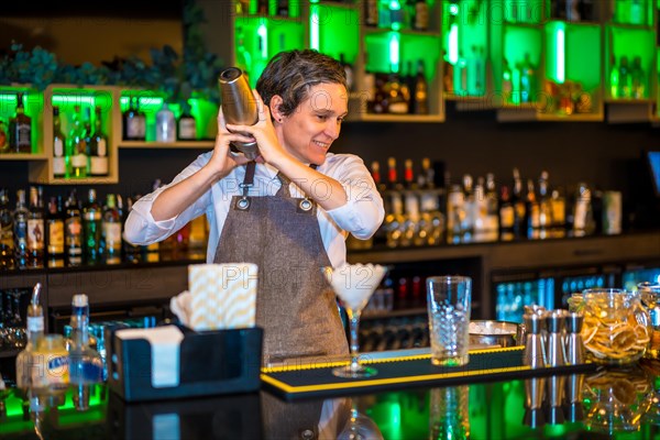 Bartender using a shaker to mix ingredients of a cocktail standing on a counter of a luxury bar