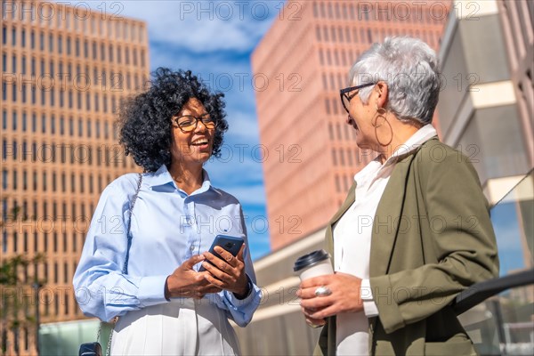 Businesswoman of different generation and ethnicity talking relaxed outdoors during a coffee break