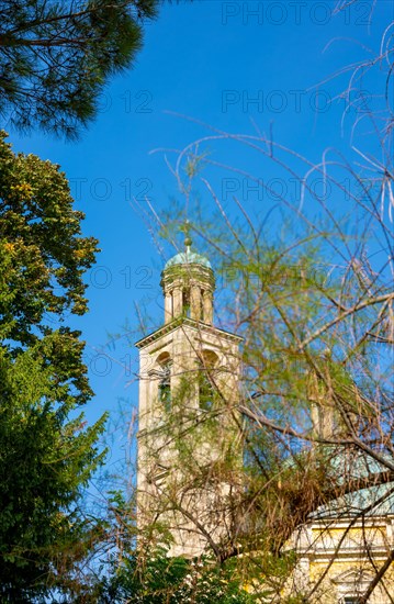 Temple of the Holy Cross with Tower Against Blue Clear Sky and Tree Branch in a Sunny Day in Riva San Vitale