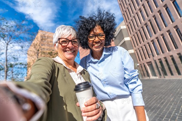 Frontal view of a mature caucasian and latin businesswomen taking a selfie outdoors