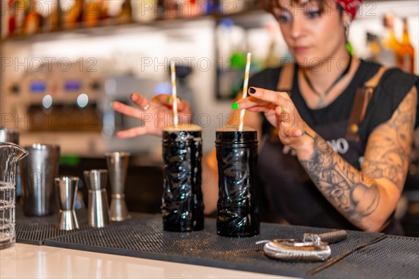 Bartender with two cocktails with straws ready to serve in the counter of a bar