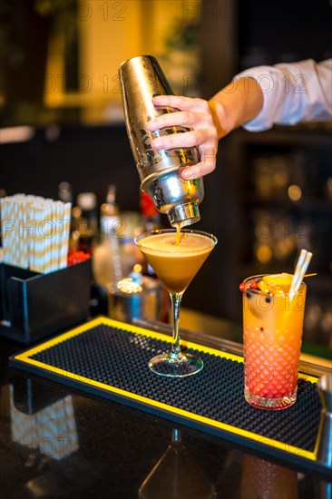 Vertical close-up of the hand of a bartender pouring a cocktail on a luxury martini glass