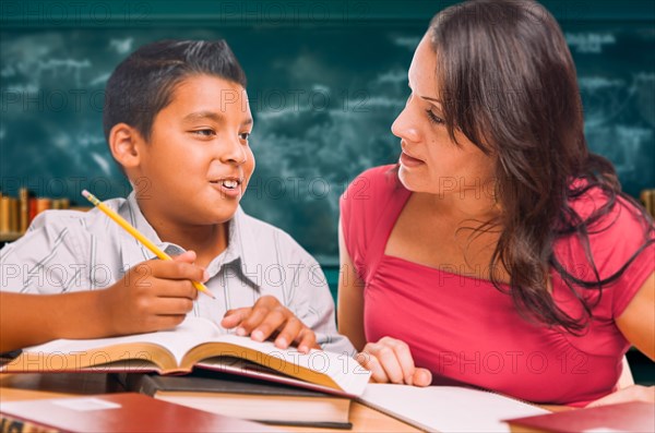 Female school teacher doing homework with a young hispanic boy in the classroom