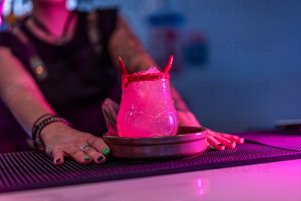 Bartender presenting a margarita cocktail decorated by devil horns in the counter of a night bar with neon lights