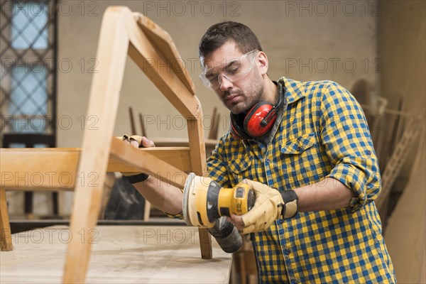 Male carpenter wearing safety glasses using sander furniture workshop