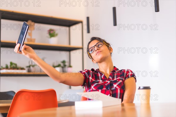 Woman taking a selfie sitting at home in a table with a book and coffee