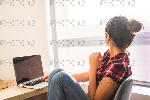 Woman looking at the window and dreaming while using laptop at home