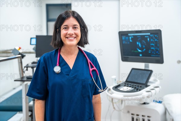 Happy cardiologist standing with arms crossed on a hospital next to modern equipment
