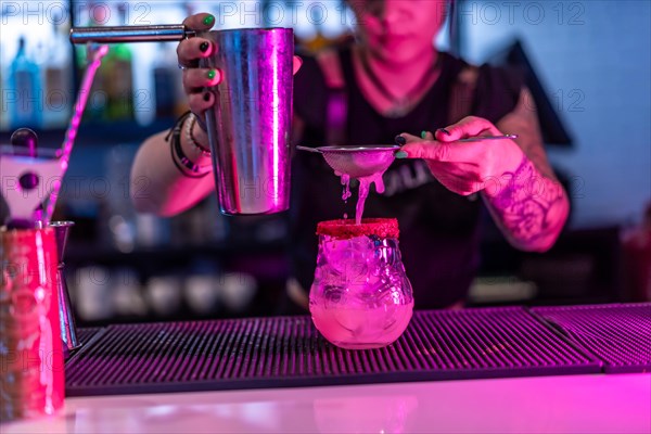Bartender pouring ingredients of a cocktail to a glass using strain