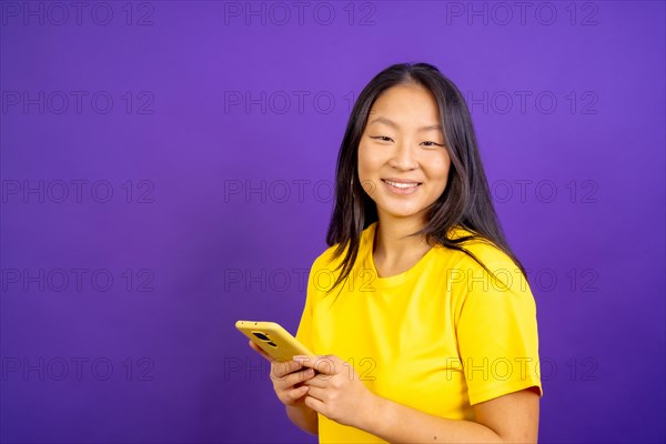 Studio photo with purple background of a chinese woman using phone and smiling at camera