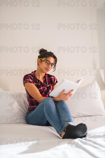 Relaxed young woman reading a book sitting on a hotel room