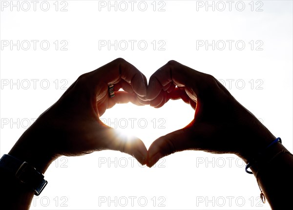 Woman Hands Making a Heart Shape Against the Sky with Sun and Sunbeam in Switzerland